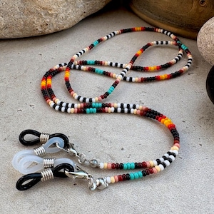May include: A beaded eyeglass chain with a colorful pattern. The chain features black, white, red, yellow, and turquoise beads. The chain has silver-colored clasps and black and clear rubber loops for holding glasses.