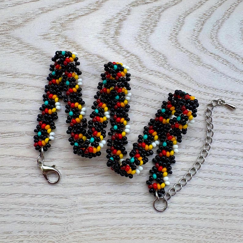 May include: A beaded bracelet with a black base, accented with red, yellow, white, and turquoise beads. The bracelet has a silver-tone clasp and an adjustable chain. The beads are tightly woven together.