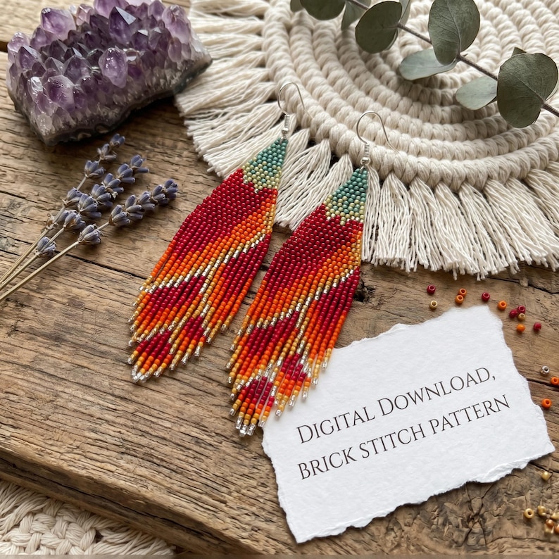 May include: A pair of long, leaf-shaped beaded earrings featuring a gradient pattern of teal, orange, red, and yellow beads. A white paper note with the text DIGITAL DOWNLOAD, BRICK STITCH PATTERN is placed next to the earrings on a wooden surface.