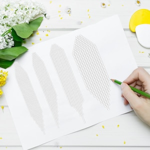 May include: A white sheet of paper with four black and white grid patterns. A hand is holding a green pencil and drawing on the paper.