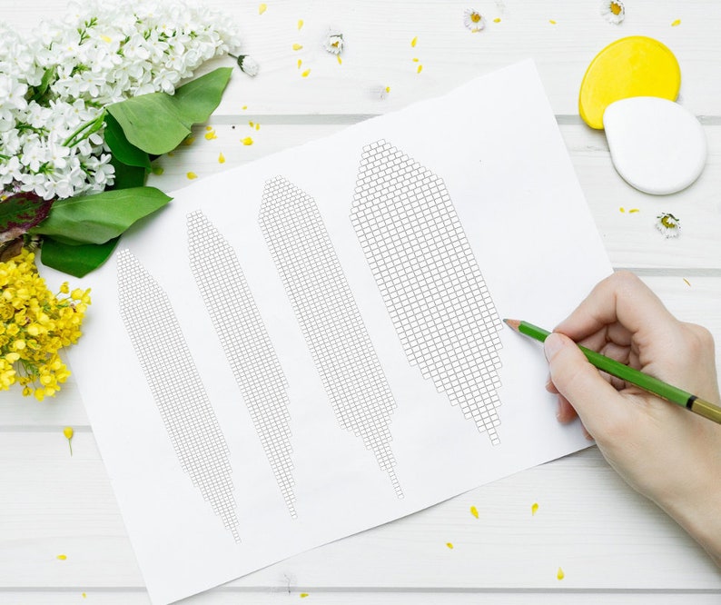 May include: A white sheet of paper with four black and white grid patterns. A hand is holding a green pencil and drawing on the paper.