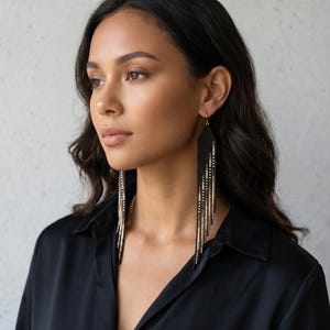 May include: Long black beaded earrings with gold accents. The earrings have a woven top and long fringe, creating a dramatic, elegant look. The gold beads are interspersed throughout the black fringe.