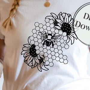 以下が含まれることがあります： ハニカムの中に2つのひまわりとミツバチが描かれた黒いデザインが施された白いTシャツ。Tシャツには円の中に「デジタルダウンロード」という文字が書かれている。「Cutting Chaos Designs」という文字がTシャツの下に書かれている。「インスタントダウンロード」という文字が「Cutting Chaos Designs」の下に書かれている。「Cricut、Silhouette、その他」という文字が「インスタントダウンロード」の下に書かれている。