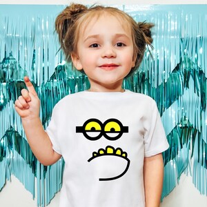 May include: A white t-shirt with a black and yellow cartoon face on the front. The face has large yellow eyes, a black mustache, and a black and white mouth.