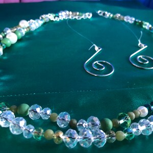 May include: A multi-strand necklace with green and white beads and a matching pair of silver earrings with a spiral design.