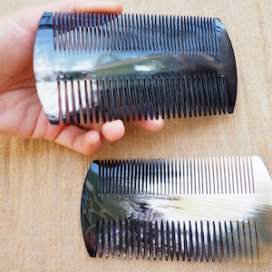 Könnte beinhalten: Zwei schwarze und weiße Hornkämme. Die Kämme haben eine abgerundete Form und sind aus natürlichem Horn gefertigt. Die Kämme sind etwa 10 cm lang.