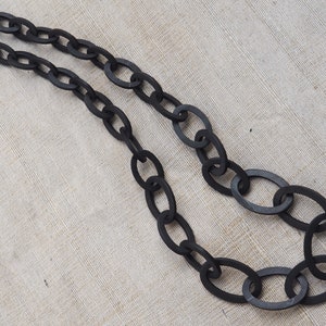 Puede incluir: Un collar de cadena negro hecho de grandes eslabones ovalados. El collar está hecho de un material liso y mate.