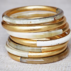May include: A stack of gold and white bangles. The bangles are made of a smooth, polished material and have a simple, elegant design.