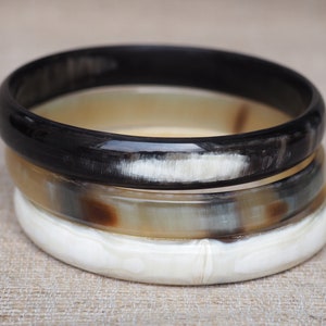 May include: Three stacked horn bangles, one black, one brown and white, and one white.