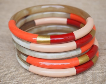 May include: A stack of four colorful bangles with a red, gold, and peach design. The bangles are made of a natural material and have a glossy finish.