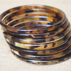 May include: A stack of brown and black tortoiseshell bangles. The bangles are made of a smooth, shiny material and have a mottled pattern.