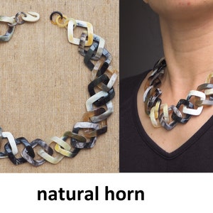 Puede incluir: Un collar grueso de cuerno natural con un diseño de eslabón de cadena. El collar está hecho de piezas de cuerno negro, blanco y marrón.