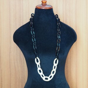 May include: A long, chunky necklace displayed on a black mannequin. The necklace features large, oval links in alternating colors: black and cream. The necklace is a statement piece, suitable for various outfits.