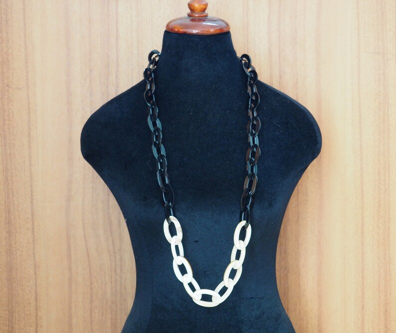 May include: A long, chunky necklace displayed on a black mannequin. The necklace features large, oval links in alternating colors: black and cream. The necklace is a statement piece, suitable for various outfits.