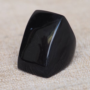 Könnte beinhalten: Ein schwarzer, geometrisch geformter Ring aus poliertem Horn.
