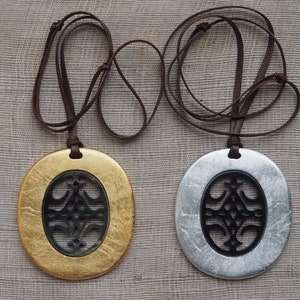 May include: Two oval pendants with a black cutout design, one with a gold finish and the other with a silver finish, hanging on brown cords.
