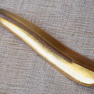 May include: A brown and gold hair comb with a gold leaf design. The comb is made of a smooth, polished material and has a curved shape.