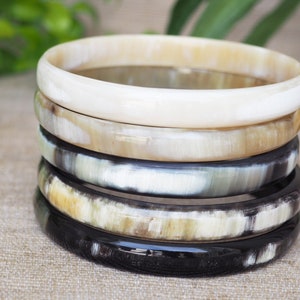 May include: A stack of five horn bangles in various shades of brown, black, and white. The bangles are made of polished horn and have a smooth, glossy finish.
