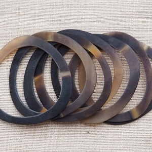 Könnte beinhalten: Ein Satz von acht braunen und schwarzen Hornarmbändern. Die Armbänder sind übereinander gestapelt und in einem Kreis angeordnet.