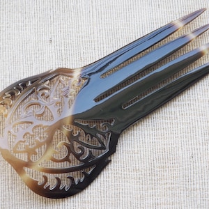 May include: A brown and black tortoiseshell hair comb with a decorative, intricate, cut-out design. The comb has four teeth.