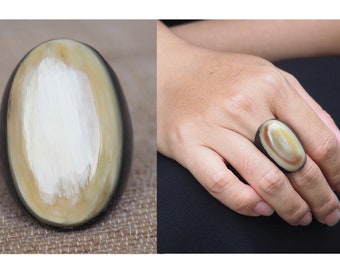 May include: A large oval ring made of dark brown horn with a light brown and white oval inlay.