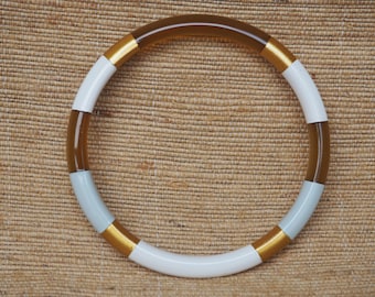 May include: A round, brown, white, and gold bangle bracelet. The bracelet is made of a smooth, hard material and has a glossy finish.