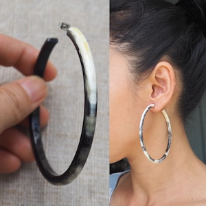 May include: A pair of large hoop earrings made of black and white horn. The earrings are round and have a smooth, polished finish.