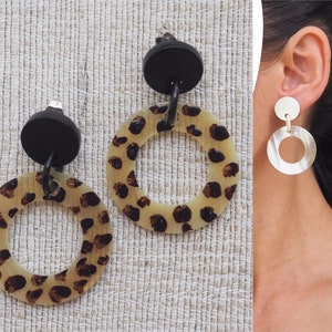 May include: A pair of dangle earrings with a black top and a large round, cream-colored disc with a leopard print pattern.