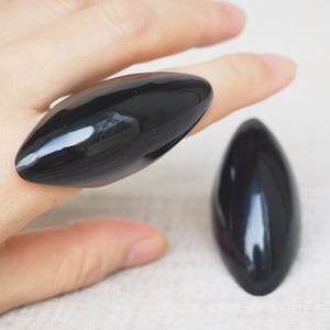 May include: Two black, glossy, oval-shaped rings. The ring on the left is worn on a finger.