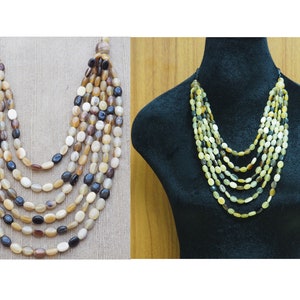 May include: A multi-strand necklace made of oval-shaped horn beads in shades of brown, beige, and black. The necklace is layered and has a cascading effect.