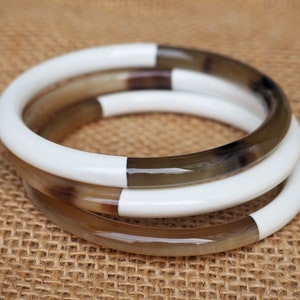 May include: Three stacked bangles made of brown and white horn. The bangles are polished and have a smooth finish.
