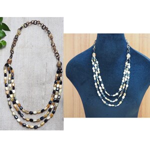 May include: A multi-strand necklace made of oval-shaped beads in shades of brown, black, and white. The necklace is displayed on a mannequin and on a flat surface.