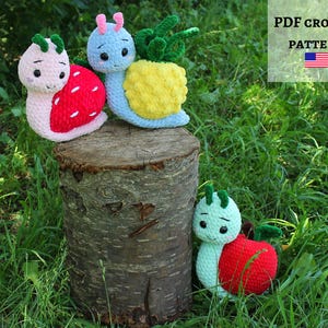 Puede incluir: Tres juguetes amigurumi de caracol hechos a crochet. Los caracoles están hechos con hilo de diferentes colores y tienen diferentes conchas de frutas y verduras. Los caracoles están sentados en un tocón de árbol en un área cubierta de hierba. PDF CROCHET PATTERN está escrito en un cartel sobre los caracoles.