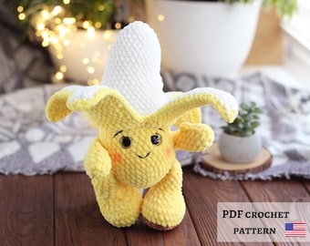 May include: A handmade crochet banana plushie with a smiling face, rosy cheeks, and brown feet. The banana peel is yellow with white accents, and the banana itself is white. The image includes the text "PDF CROCHET PATTERN" and the American flag.