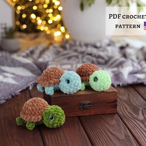 May include: A collection of handmade crochet turtle toys in various colors, including brown, blue, and green. The turtles are displayed on a wooden box. The image also includes text that reads "PDF CROCHET PATTERN" with the American flag.
