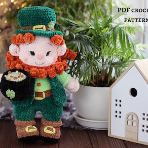 Pode incluir: Boneca de duende de crochê feita à mão, segurando um pote de ouro. A boneca está vestida de verde e marrom, com um chapéu verde e barba laranja. Padrão de crochê em PDF.