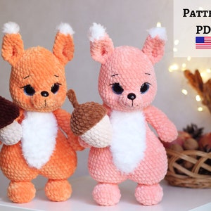 May include: Two crocheted plush squirrel toys, one orange and one pink, holding a brown crocheted acorn and mushroom. The toys have white fur on their bellies and black eyes.  PATTERN PDF.