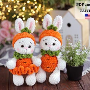 May include: Two handmade white crochet bunny dolls wearing orange carrot-themed outfits and green collars. The bunnies have pink-lined ears. The background is blurred, with the text "PDF CROCHET PATTERN" and the American flag.