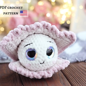 May include: A handmade white crochet doll with large, iridescent eyes and a smiling face, set within a light pink, ruffled shell. The doll is a soft, plush toy. Text on the image reads "PDF CROCHET PATTERN" with a US flag.