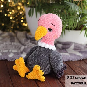 May include: A handmade crochet vulture with a pink head, yellow beak, and gray body. The vulture has a white collar and is sitting on a wooden surface. Two yellow crochet feet are in front of the vulture. Text on the image reads "PDF CROCHET PATTERN".