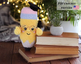 May include: A handmade crochet pencil doll wearing glasses and a graduation cap, with a smiling face. The pencil is yellow, pink, and blue, and is sitting on top of a stack of old books. The text "PDF CROCHET PATTERN" is visible in the image.