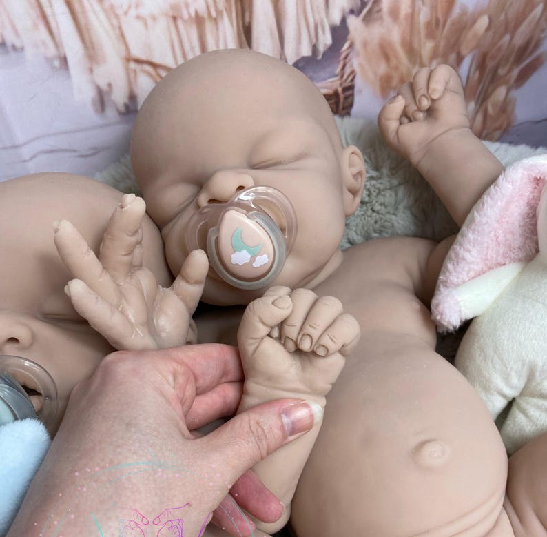 May include: Two realistic baby dolls with closed eyes and pacifiers in their mouths. The dolls are made of soft, lifelike silicone and have detailed features, including tiny fingers and toes.