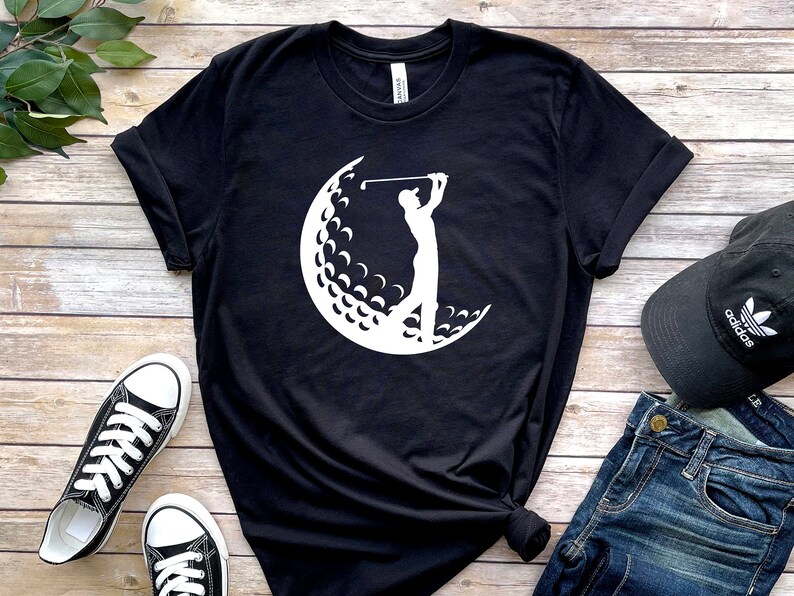 May include: Black t-shirt with a white silhouette of a golfer swinging a club in front of a golf ball.