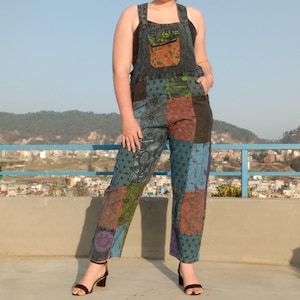 May include: Patchwork denim dungarees with a blue, green, brown and purple colour scheme. The dungarees have a large pocket on the front and adjustable straps.