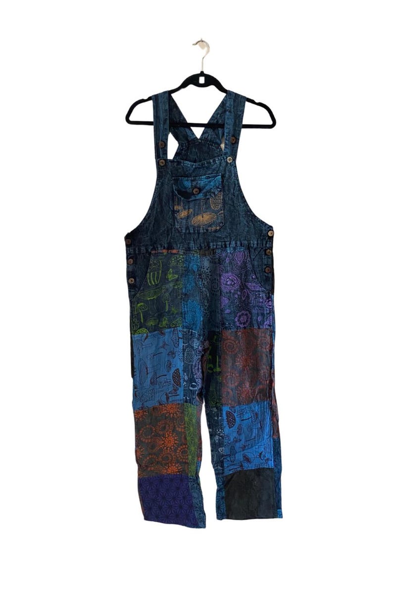 May include: Blue denim dungarees with a patchwork design featuring various colourful patterns. The dungarees have a bib with a pocket and adjustable straps.