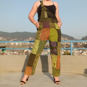 May include: Green patchwork dungarees with a black vest top. The dungarees have a variety of patterns and colours, including green, orange, purple, and brown.