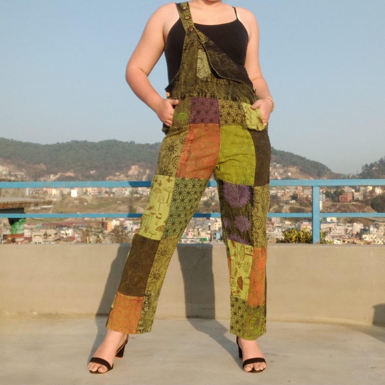 May include: Green patchwork dungarees with a black vest top. The dungarees have a variety of patterns and colours, including green, orange, purple, and brown.