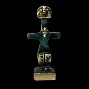 May include: A small bronze sculpture of a stylized human figure with a cross on its chest. The figure is standing on a square base.