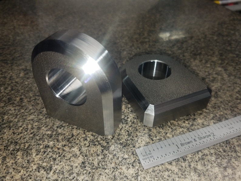 Puede incluir: Dos anillos de elevaci&oacute;n de metal, uno con forma redondeada y el otro con forma cuadrada. Ambos tienen un agujero central para un gancho de elevaci&oacute;n.