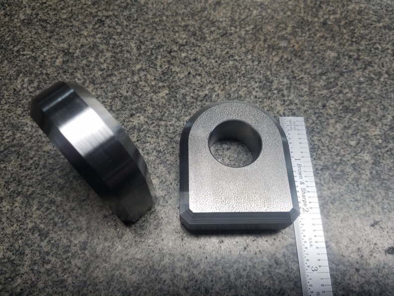 Puede incluir: Dos anillos met&aacute;licos, uno con un agujero redondo y el otro con forma de D, se muestran junto a una regla. La regla est&aacute; marcada con pulgadas y el texto "Brown & Sharpe 2".
